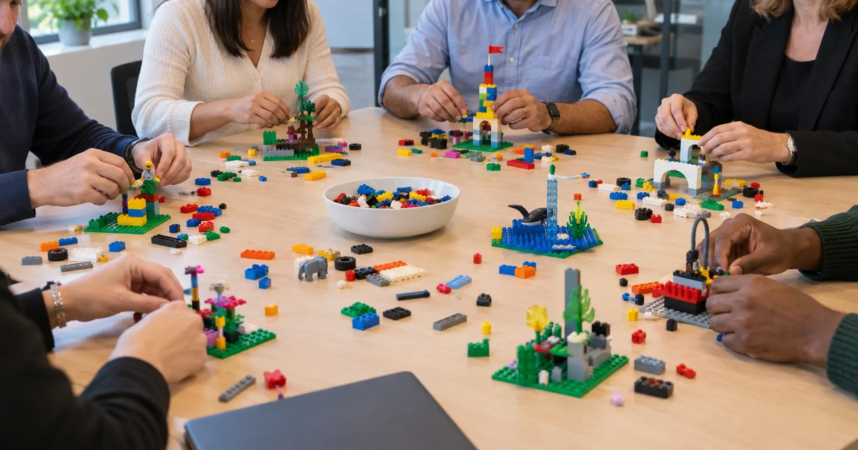 Two groups of colleagues from merging companies building separate LEGO® SERIOUS PLAY® models of their working culture at a shared table